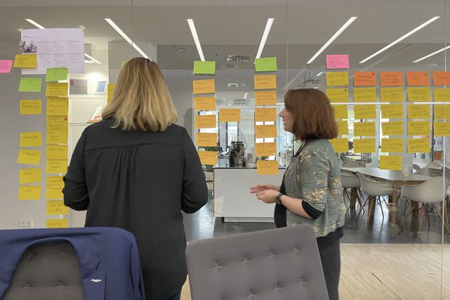 Zwei Personen stehen vor einer Glasscheibe mit Post-Its.