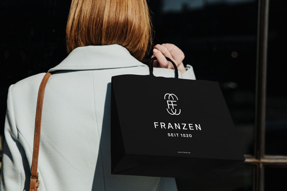 Eine Person trägt eine schwarze Papiertragetasche von Franzen über der Schulter.