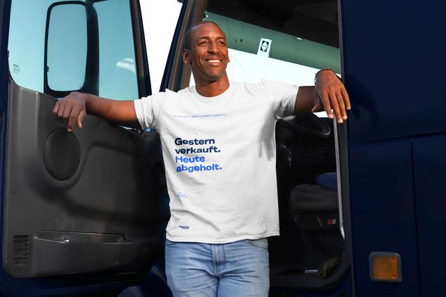 Ansicht von einem Mann in einem weißen Copart-Tshirt der in einer LKW-Tür lehnt und lächelnd in die Ferne schaut.
