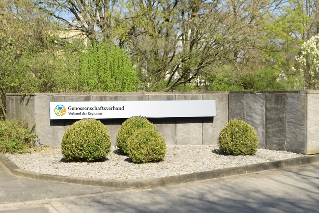 Auf einem Metallschild im Außenbereich ist das Logo des Genossenschaftsverbandes mit Folie aufgebracht