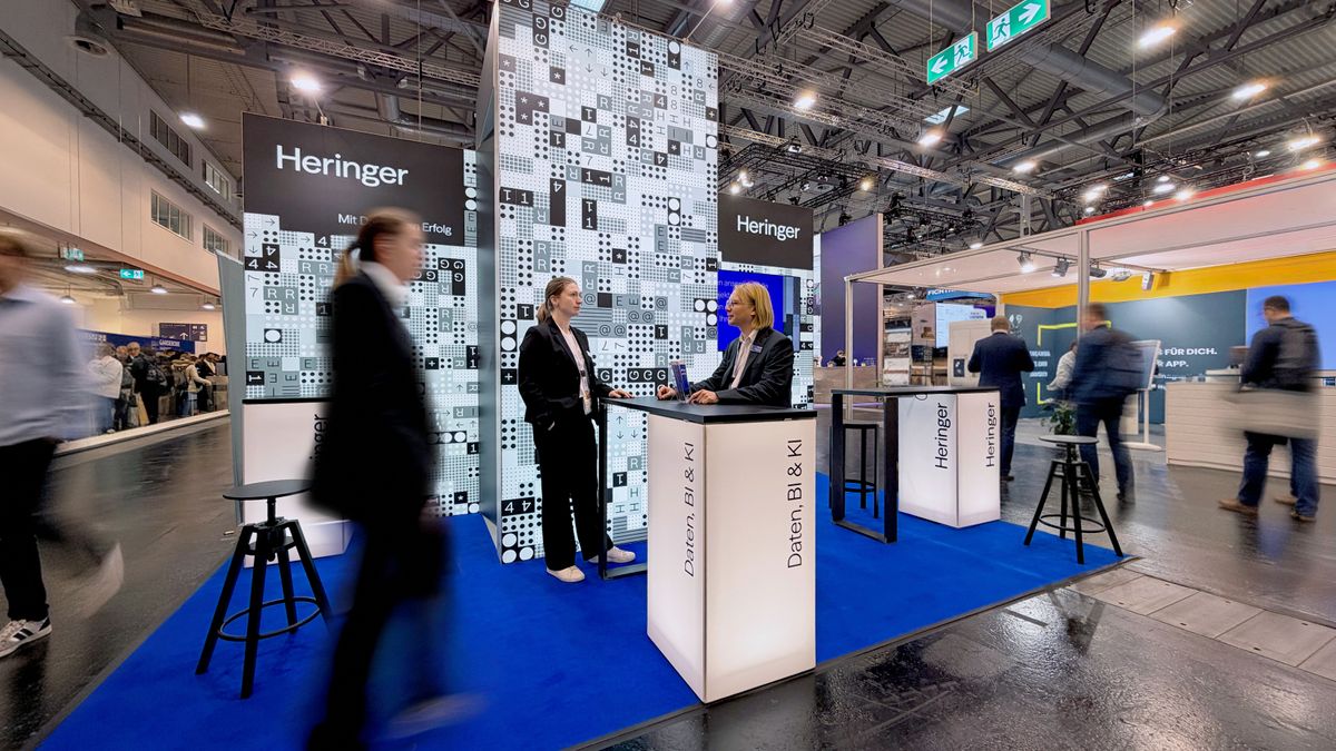 Der Messeauftritt macht Datenkompetenz und Markenidentität unmittelbar erlebbar. Realisierter Messestand von Heringer auf einer Fachmesse mit grafischen Flächen, Leuchtmöbeln und digitalen Inhalten.