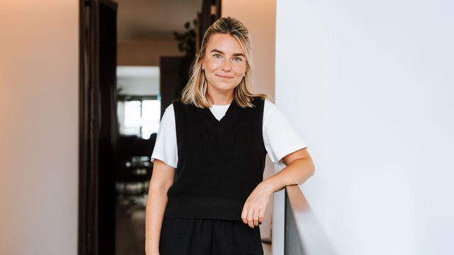 Eine Frau steht vor einem Türrahmen, angelehnt an ein Geländer und lächelt