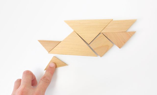 Eine Hand legt einen Fisch mit dem Holzlegespiel „Tangram“