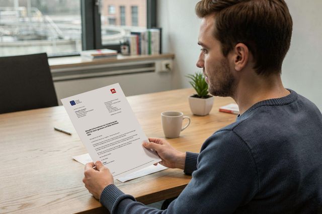 Mann sitzt an einem Schreibtisch und liest ein offizielles Schreiben in einem modernen Büro.