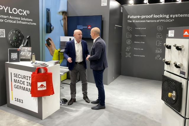 Zwei Männer unterhalten sich an einem Messestand eines Industrieunternehmens mit ausgestellten Produkten und Branding-Elementen.