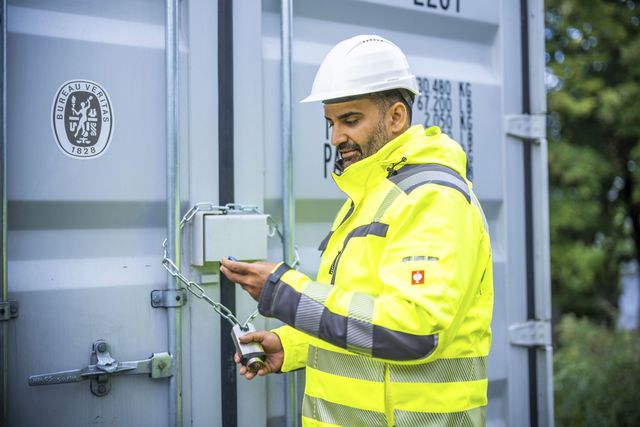 Mitarbeiter in Schutzkleidung sichert einen Container mit einem Schloss und überprüft die Verriegelung.