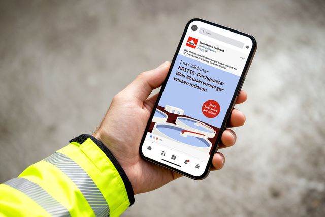 Person in Arbeitskleidung hält ein Smartphone mit einer Social-Media-Anzeige für ein Webinar eines Industrieunternehmens.