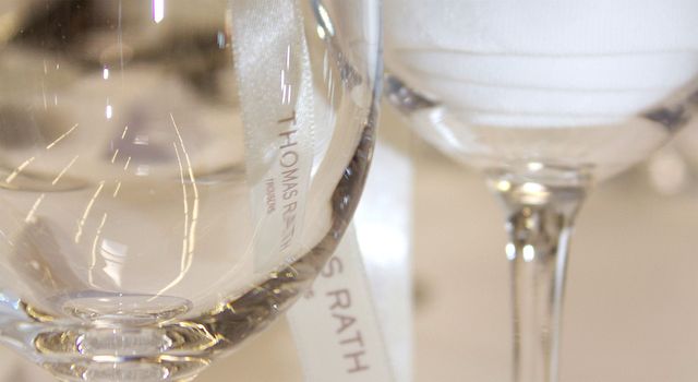 Ein Satinband mit Logobestickung liegt in einem Weinglas