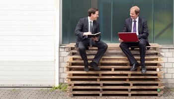 Zwei Männer sitzen auf Holzpaletten und unterhalten sich