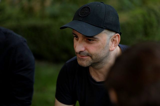 Mehrere Personen sitzen im Grünen, eine davon ist im Fokus.