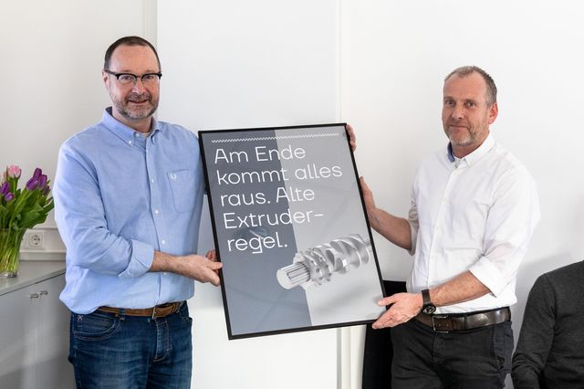 Geschäftsführer von Extruder Experts halten ein Poster im neuen Corporate Design hoch