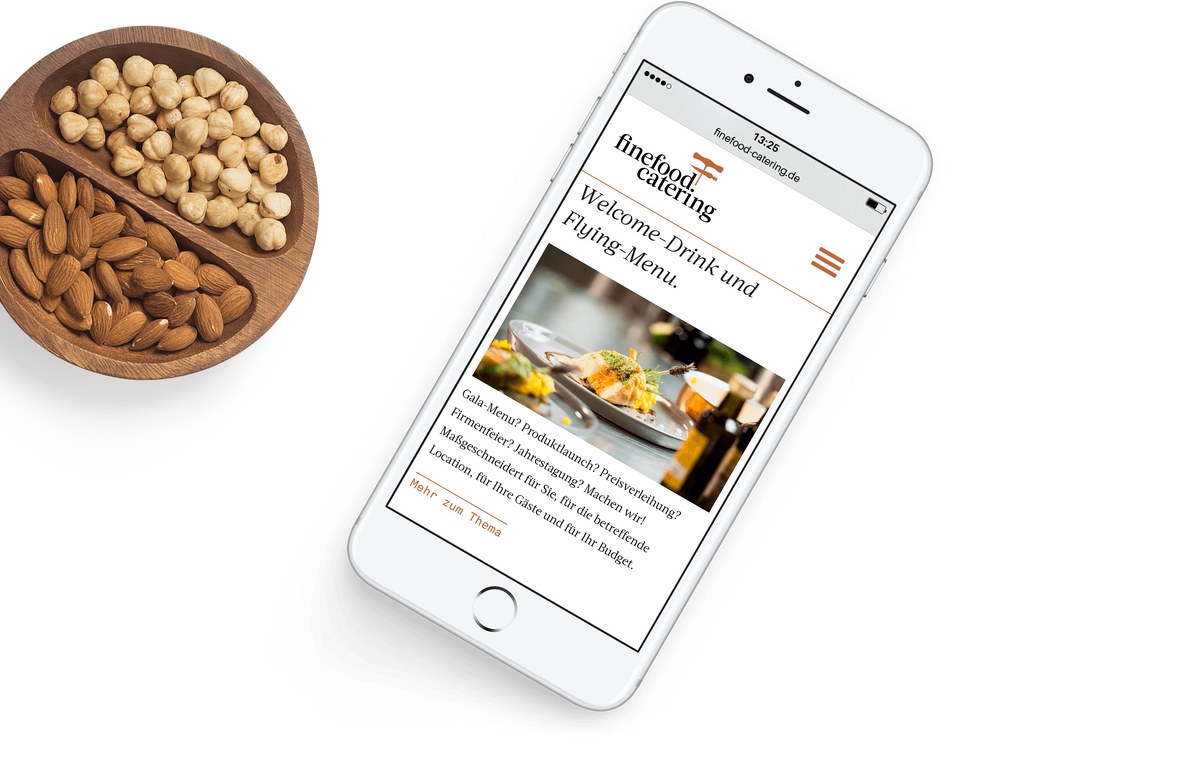Smartphone mit der finefood-Website auf der eine Foodfotografie und ein Text über die maßgeschneiderten Services zu sehen ist neben einer mit Nüssen gefüllten Schale