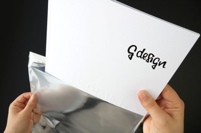Person packt das G Design Lookbook aus einer silbernen Versandtasche aus