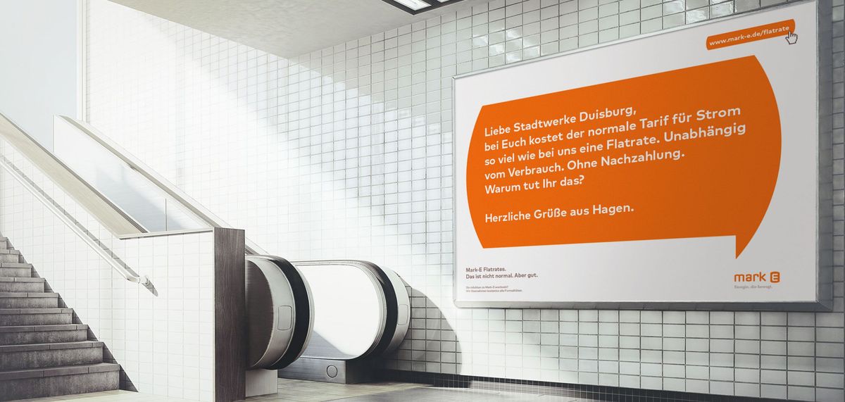 Großformatiges Plakat mit Mark-E-Werbemotiv auf einer Wand neben einer Rolltreppe
