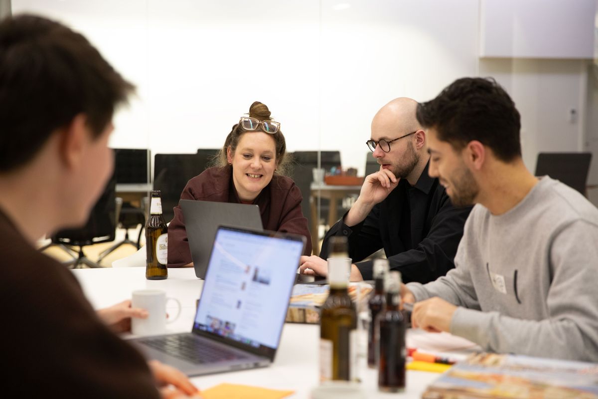 Im Vordergrund sitzt eine Person, während sich im Fokus drei weitere Personen angeregt unterhalten