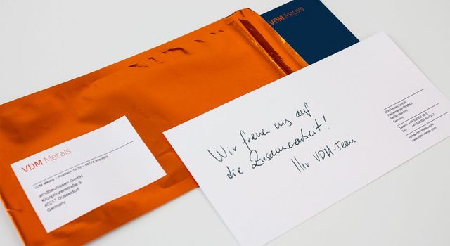 Eine Grußkarte liegt auf einem orangenem Folien-Kuvert